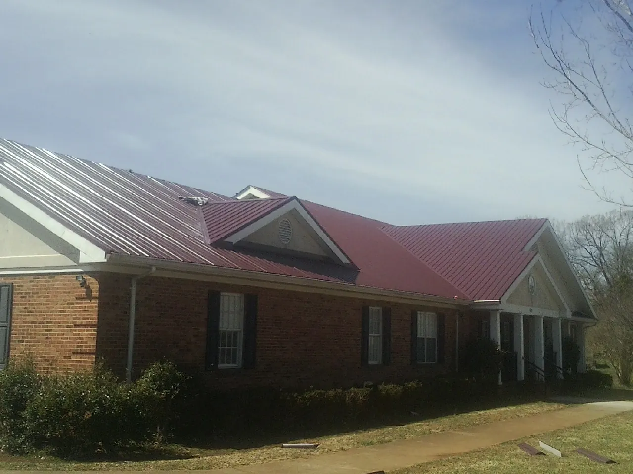 Red metal roof with gabled entries on a long brick building, from a Hail Damage Roof Repair job in Claymont