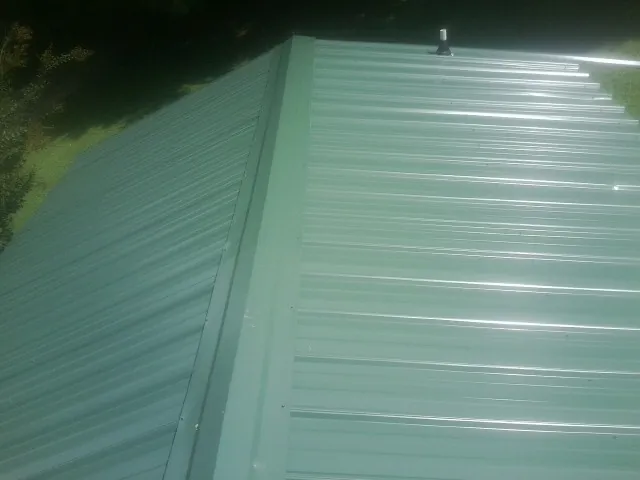 New green metal panels meeting at the ridge of a roof — Flat Roof Repair work by our crew in Claymont