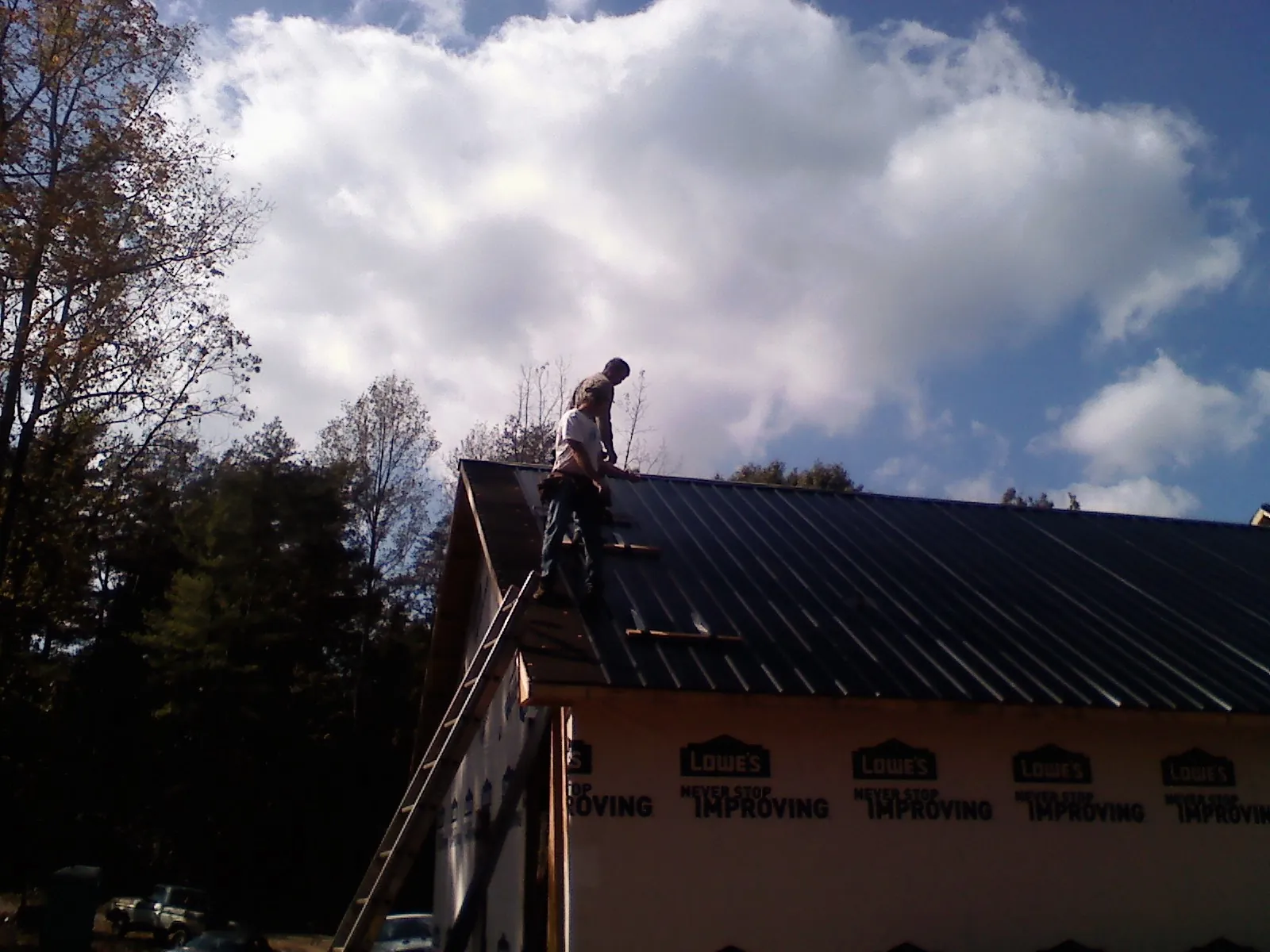 Roofer fastening dark metal panels high against a cloudy sky, from a Roof Inspection job in Claymont