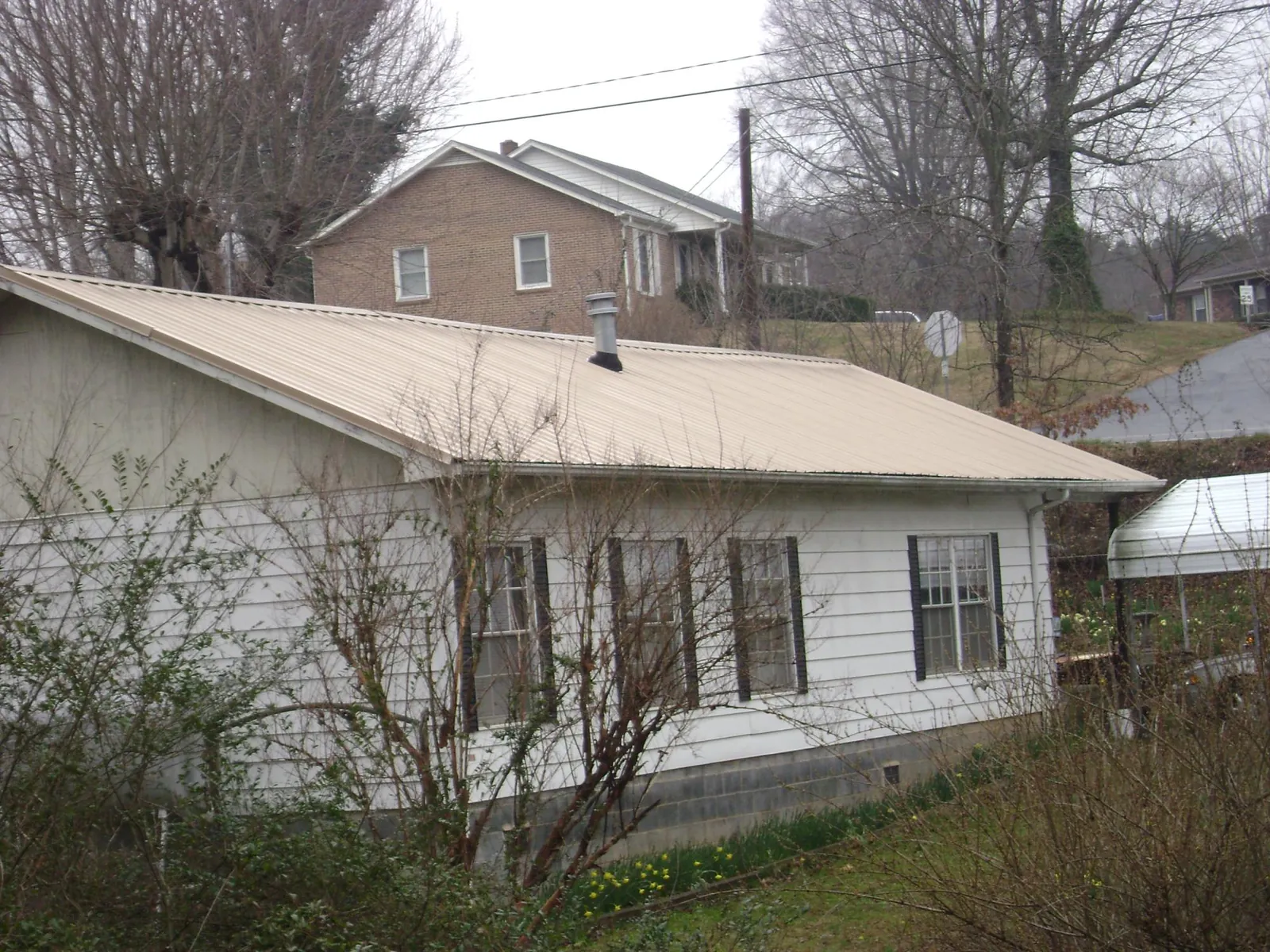 Tan metal roof on a white sided house set into a hillside — Commercial Roofing by Roofing Brothers in Claymont